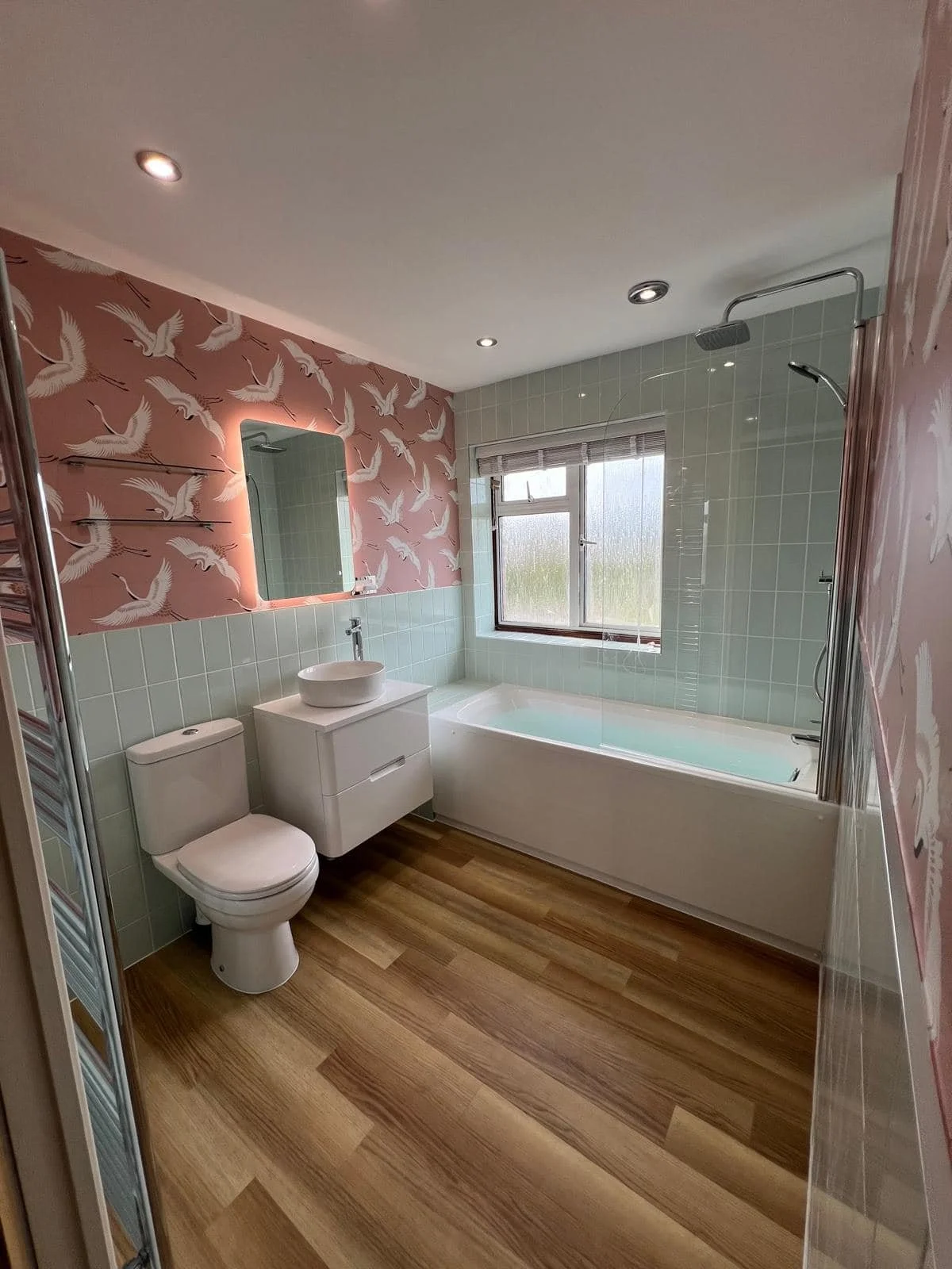 Bathroom with bird-patterned wallpaper, green wall tiles, bath and wood-effect flooring