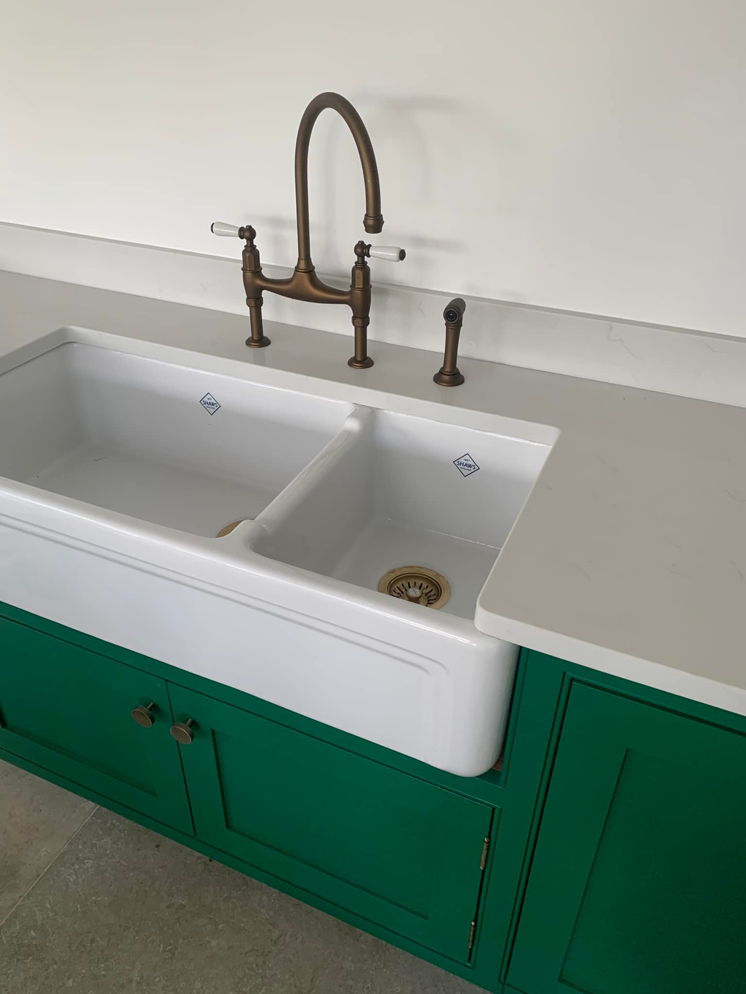 Farmhouse-style kitchen sink with brass tap and green cabinet