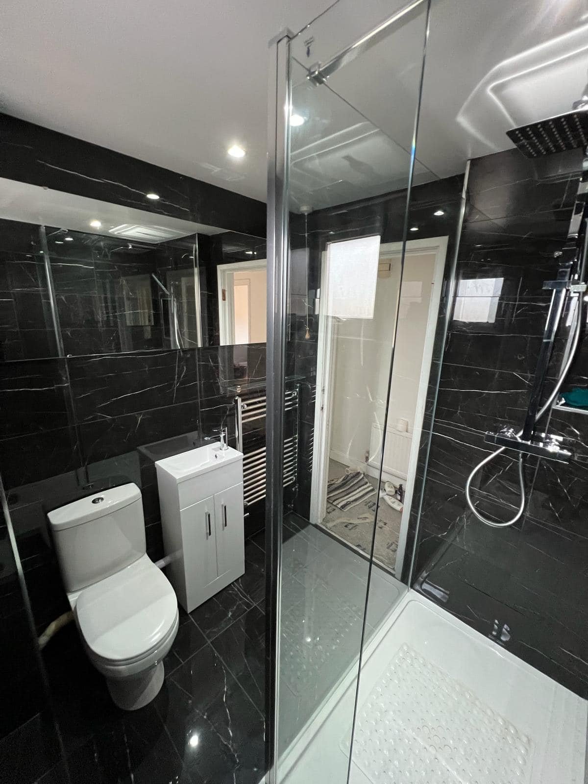 Black marble shower room with toilet, vanity, towel rail and glass shower enclosure