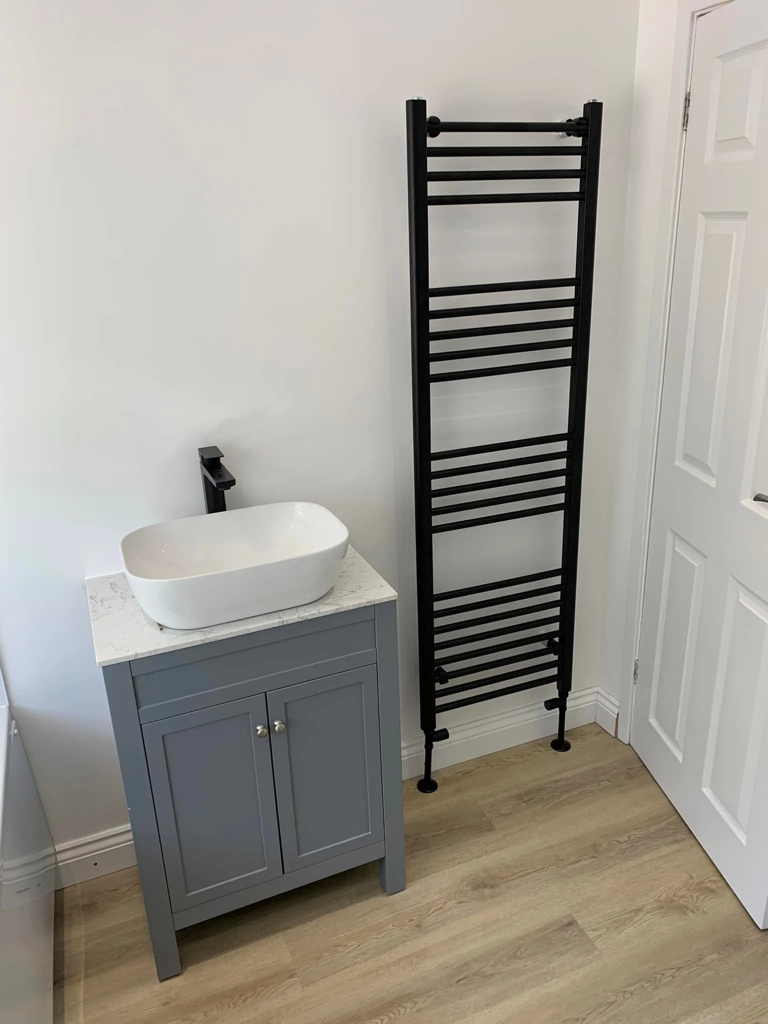 Finished wet-room with grey vanity, vessel basin and black heated towel radiator