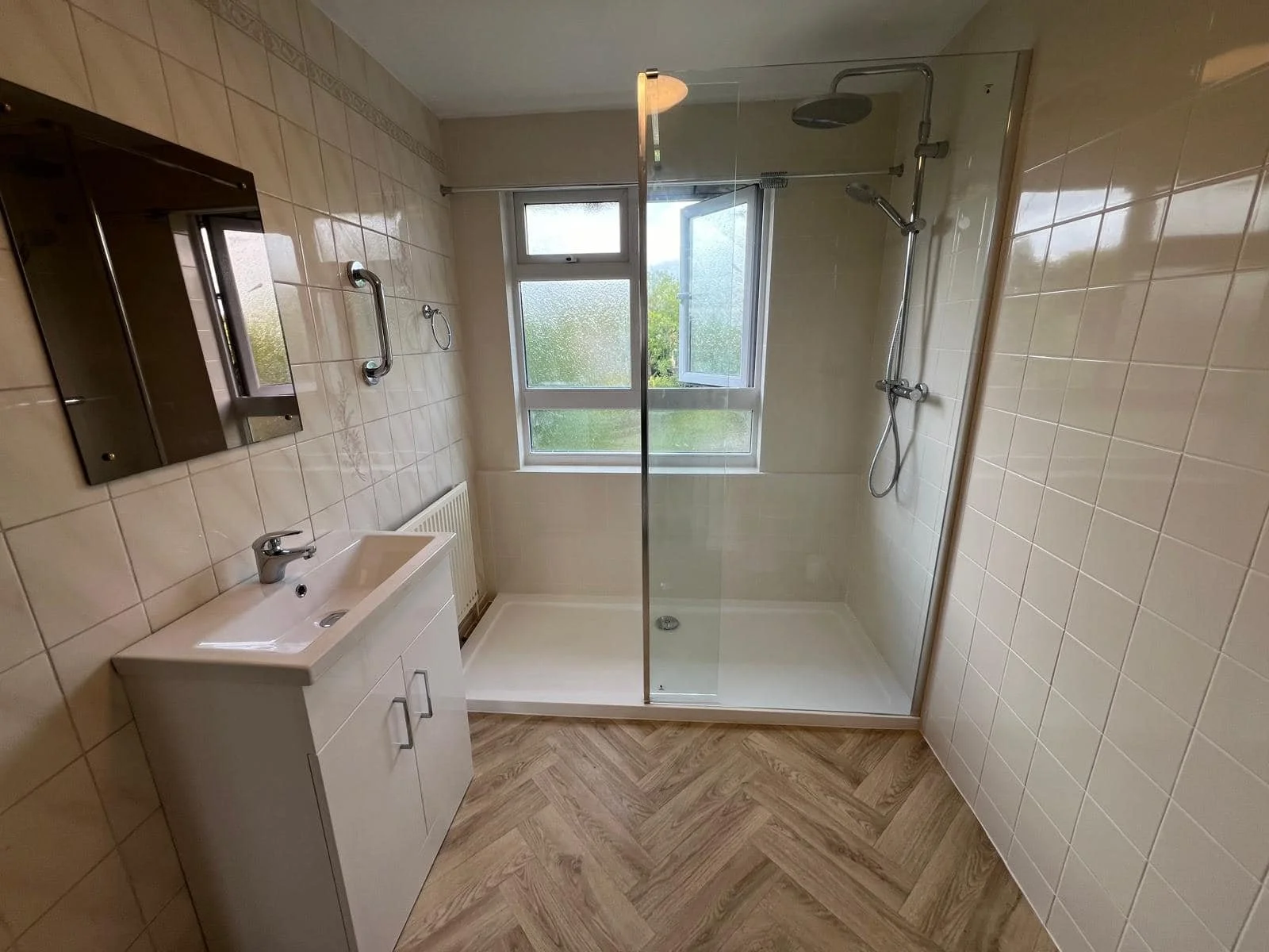 Finished wet-room with walk-in shower, white vanity and herringbone floor