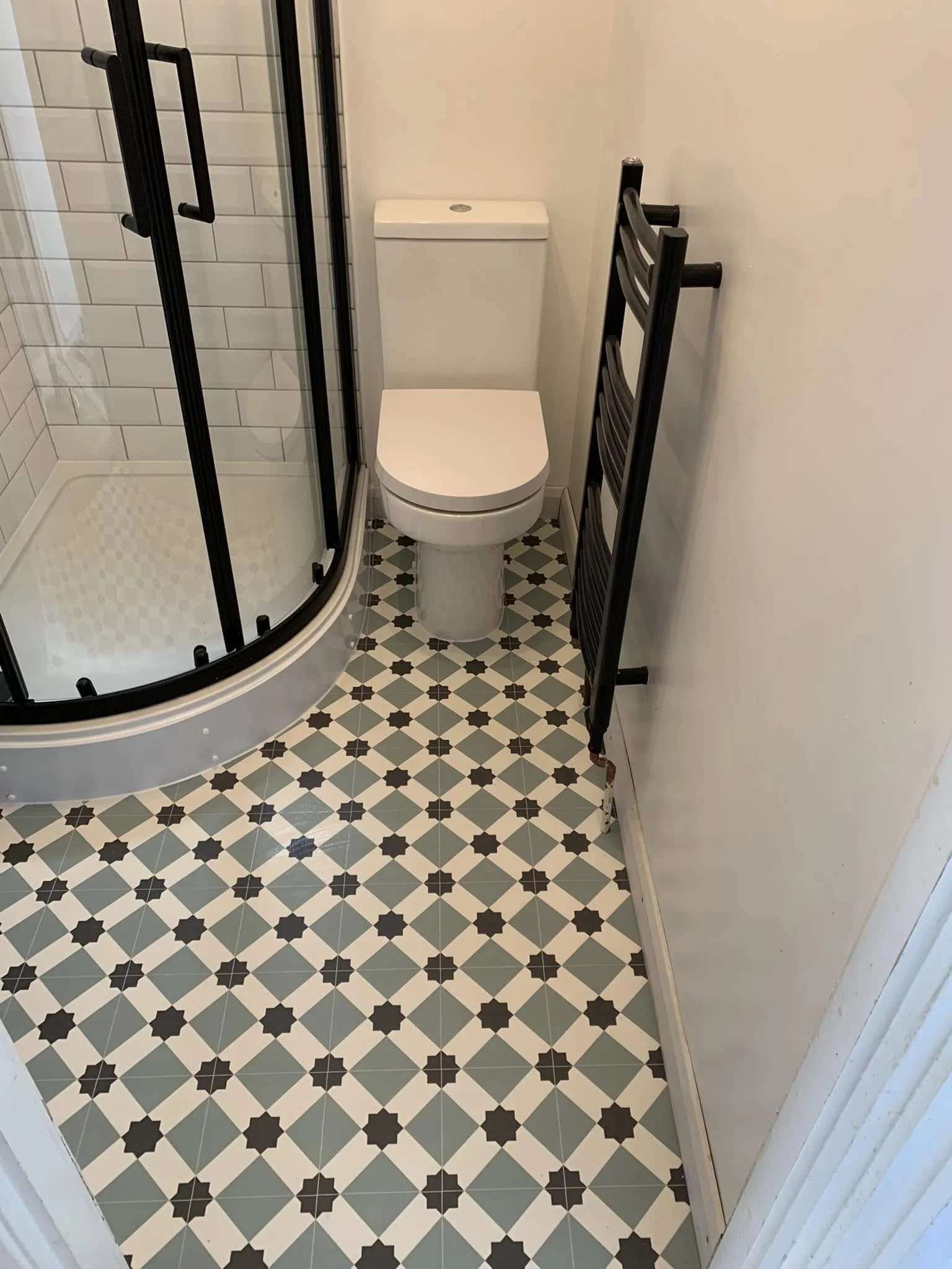 Shower room with patterned floor tiles, toilet, corner shower and black towel radiator
